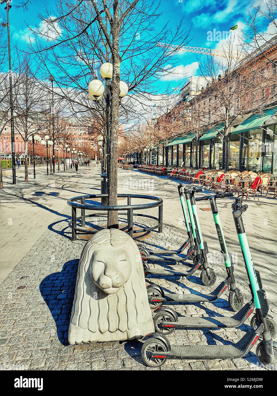 Stone lion carving electric scooters and line of cafes and terraces, Kungsträdgården, Stockholm, Sweden, Scandinavia - Smartphone Captured Stock Image