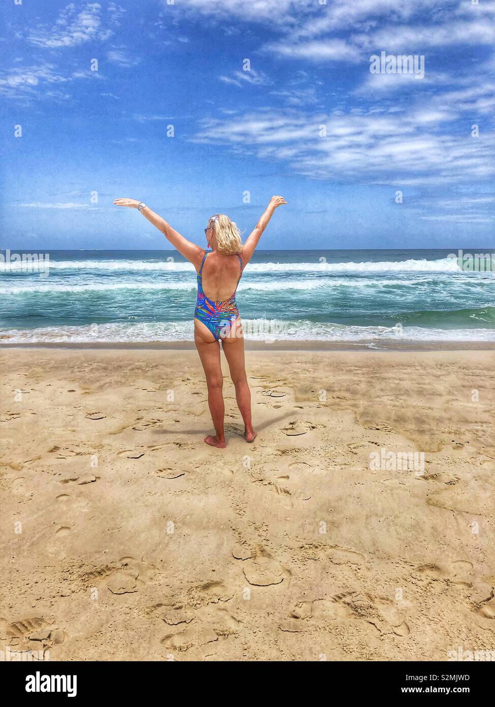 Woman standing on the beach with outstretched arms facing the sea. - Smartphone Captured Stock Image