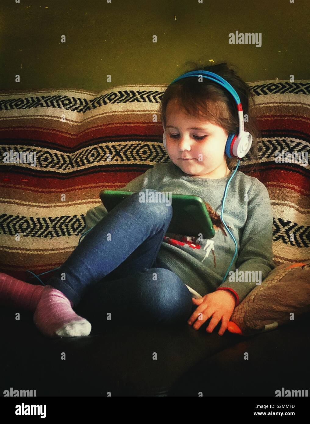 3 year old girl sitting on couch using tablet with headphones Stock Photo