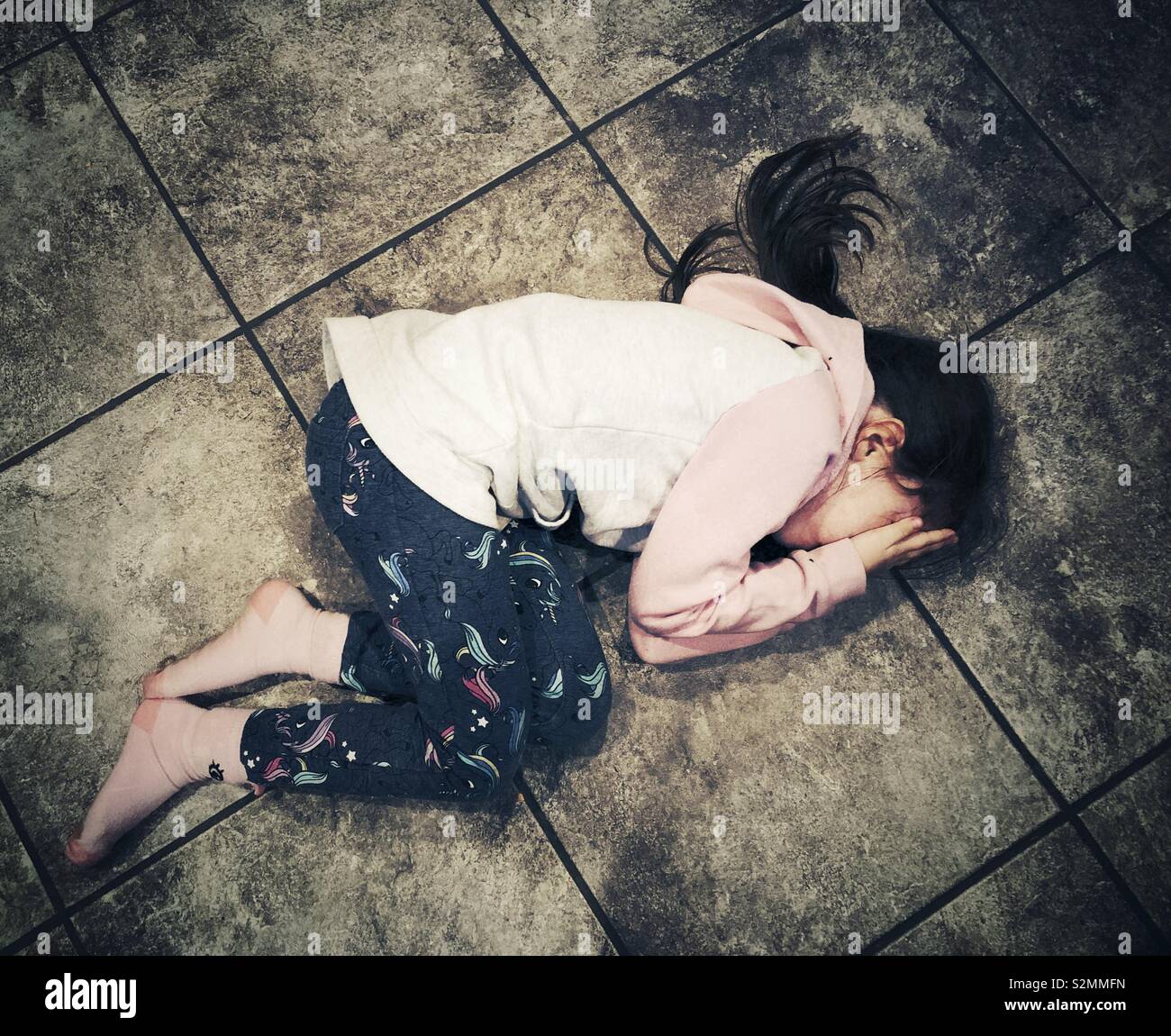 Young girl on floor covering face with hands while crying Stock Photo
