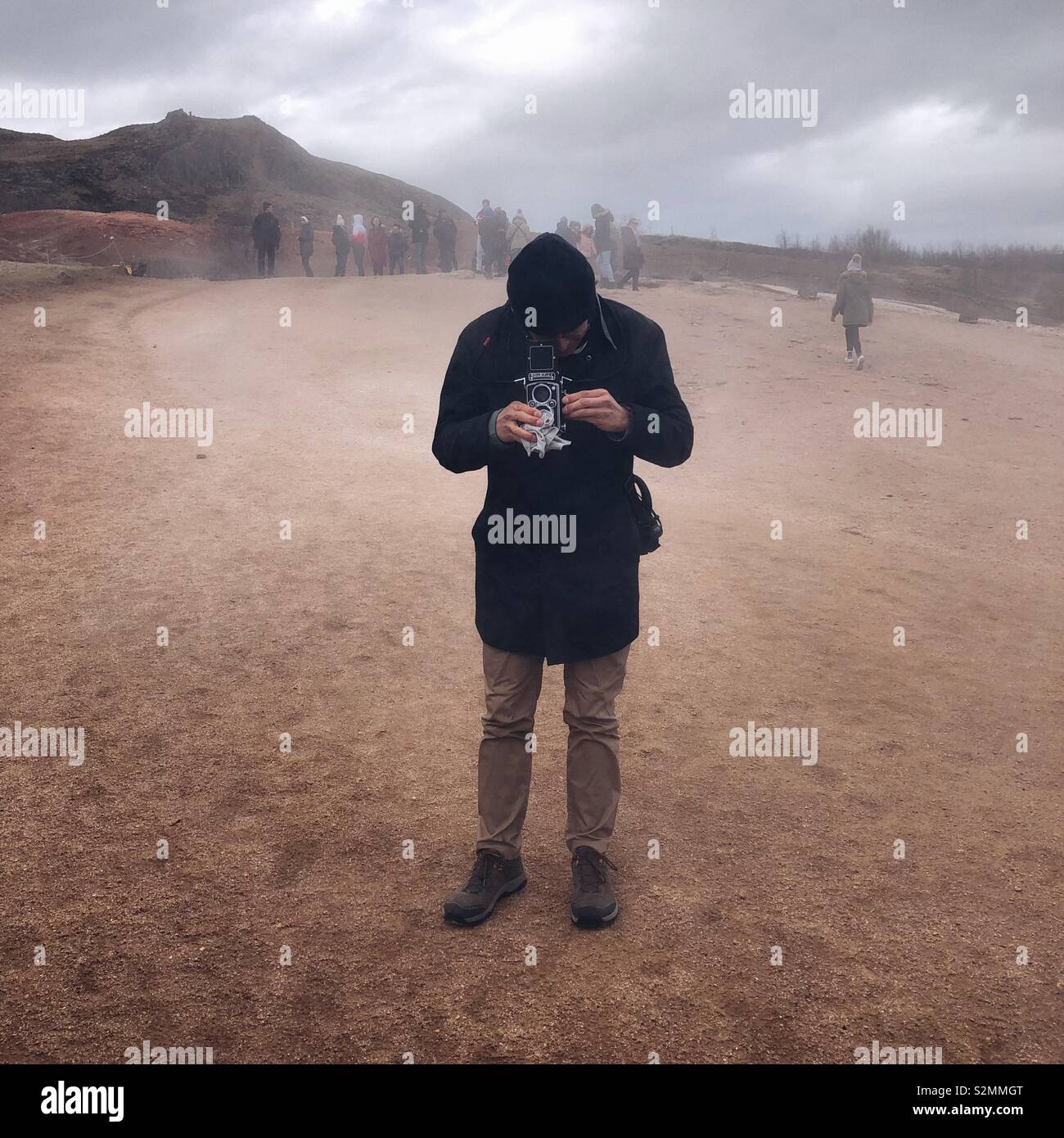 Man wiping vintage film camera lenses from geyser steam in Iceland - Smartphone Captured Stock Image