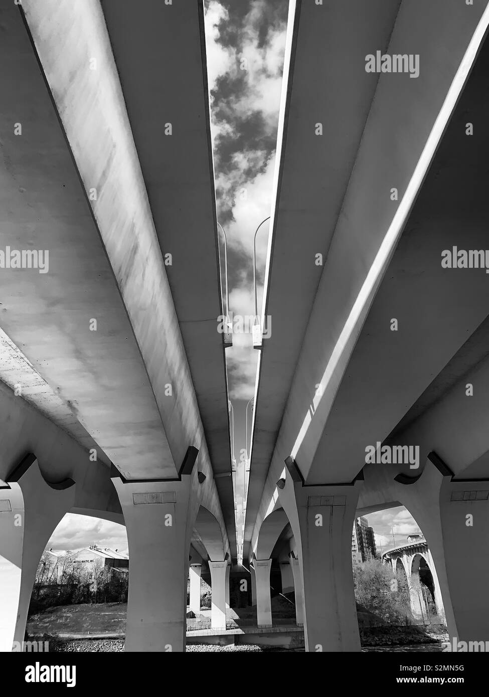 Black and white shot underneath a highway bridge that spans over a river. Stock Photo