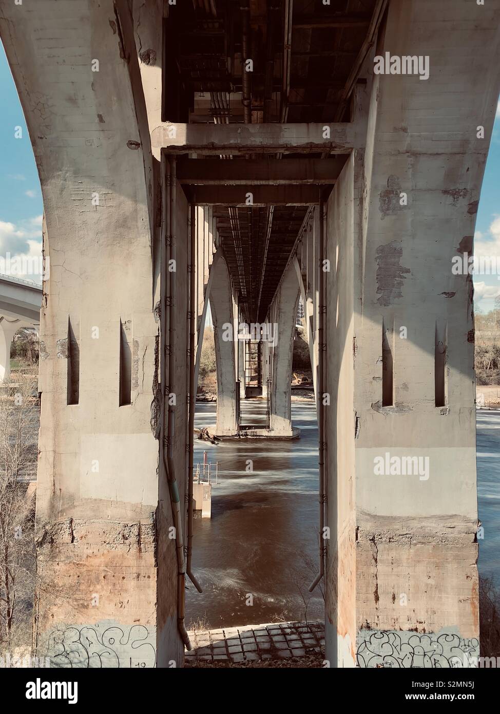 Looking underneath an old bridge that spans a large river. Stock Photo