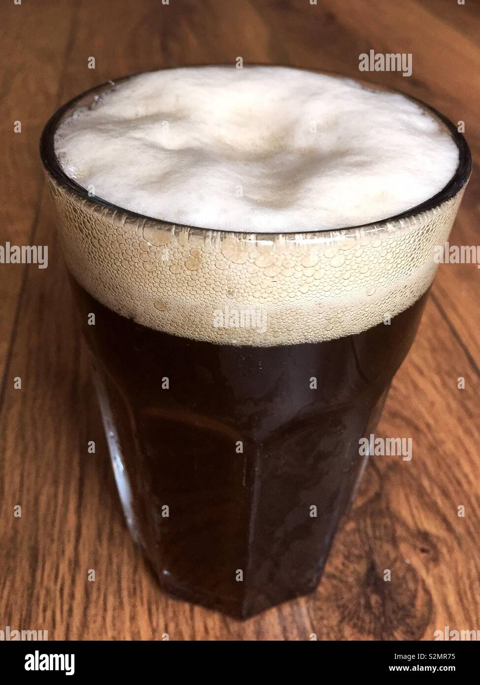 Glass or pint of ale beer with a foamy head on a wooden table - Smartphone Captured Stock Image