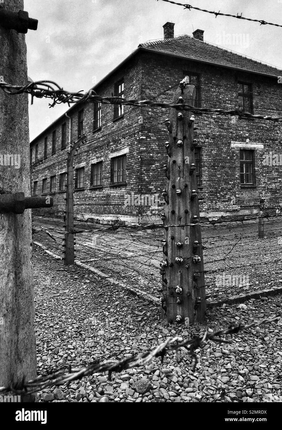 An exterior view of a building surrounded by electric fencing at the WW2 Nazi Auschwitz Concentration Camp in Oswiecim, Poland. Now a Memorial Museum & UNESCO World Heritage Site. © COLIN HOSKINS. - Smartphone Captured Stock Image