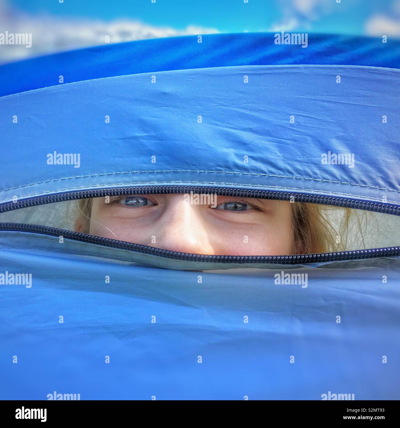 Young girl peeking out from door flap of blue tent Stock Photo