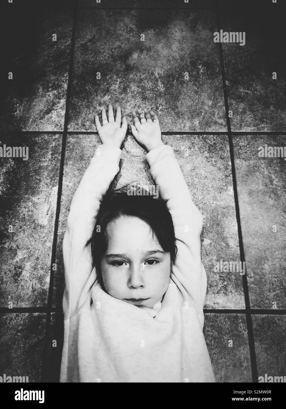 Young girl on tile floor with arms up Stock Photo