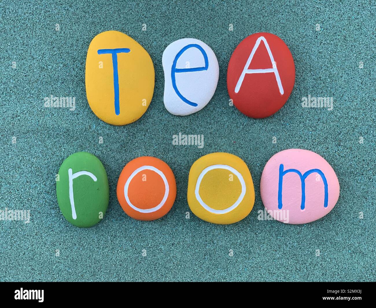 Tea room sign composed with multi colored stones over green sand Stock Photo