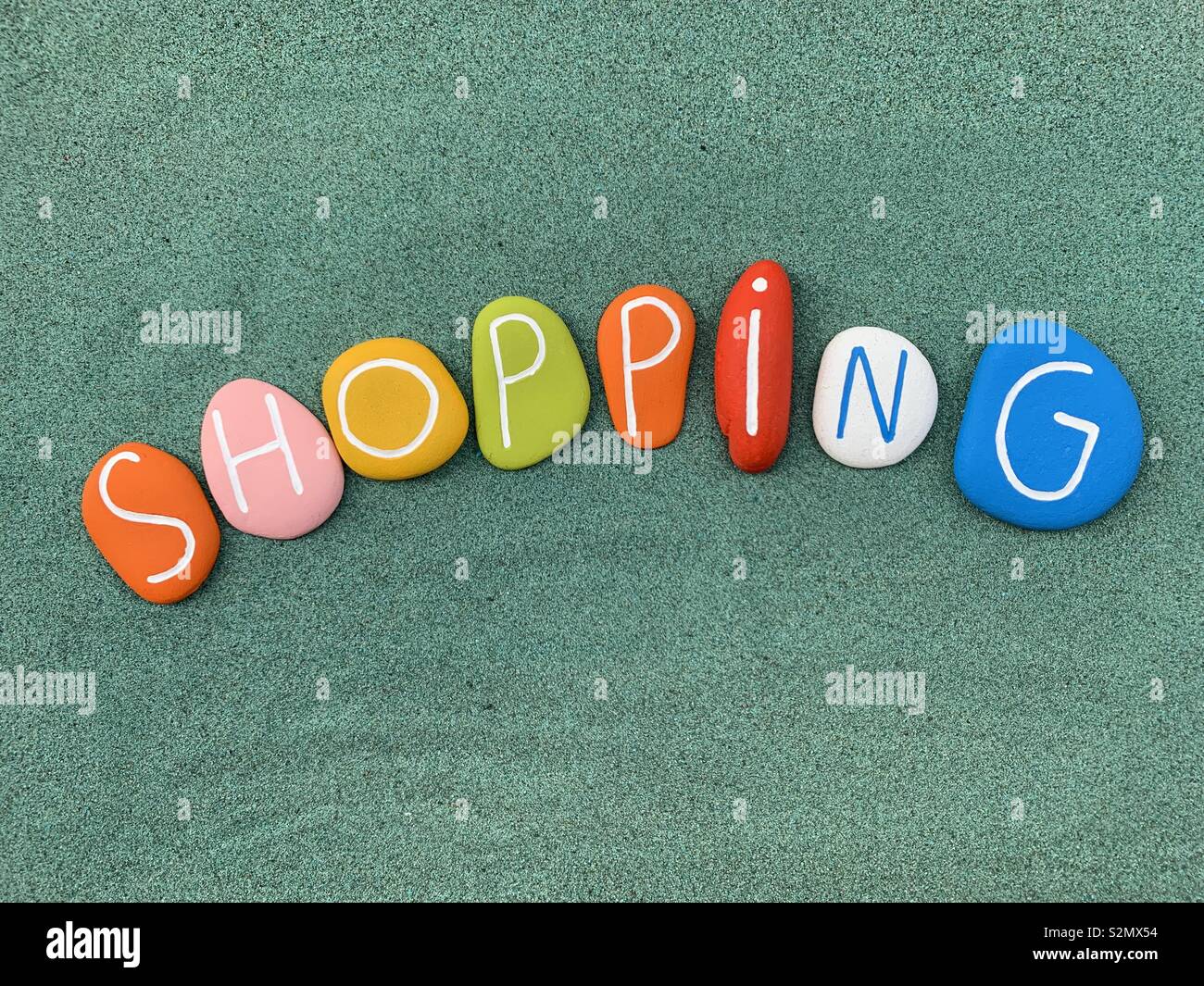 Shopping text composed with multi colored stones over green sand - Smartphone Captured Stock Image