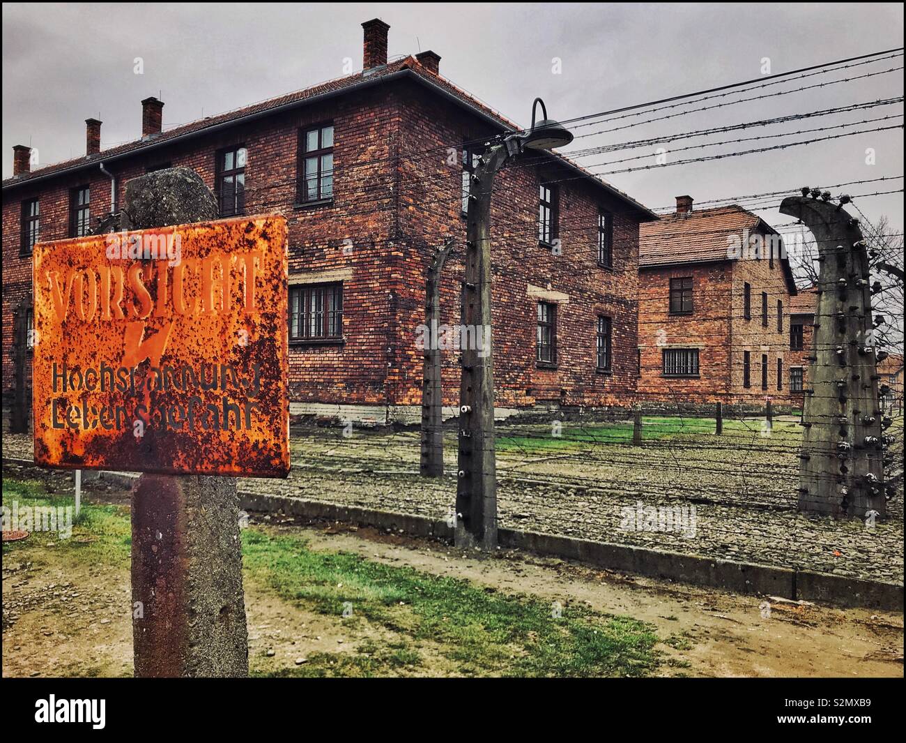 A sign @ the Nazi Auschwitz Concentration Camp warns inmates that the fence is electrified. Tens of Thousands of People (mostly Jews) were killed during here during the early 1940’s. Now a UNESCO Site Stock Photo