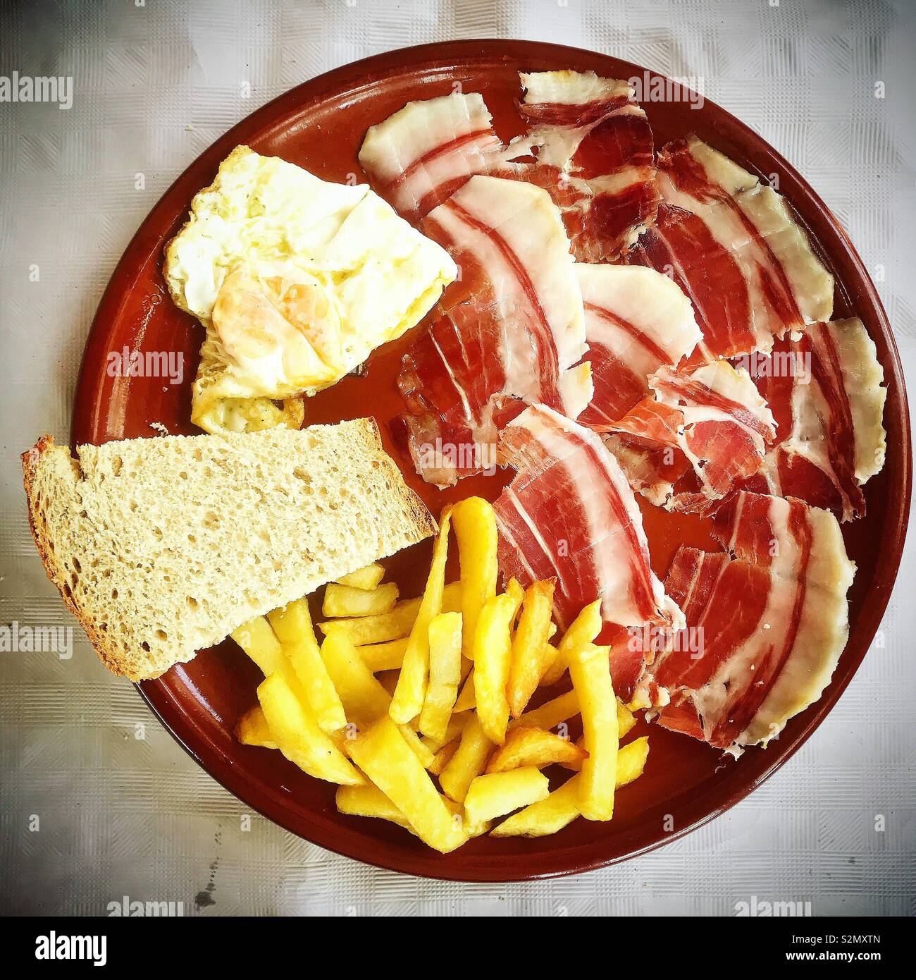 Iberian ham, a fried egg, fried potatoes and bread in a house in Prado del Rey, Sierra de Cadiz, Andalucia, Spain - Smartphone Captured Stock Image