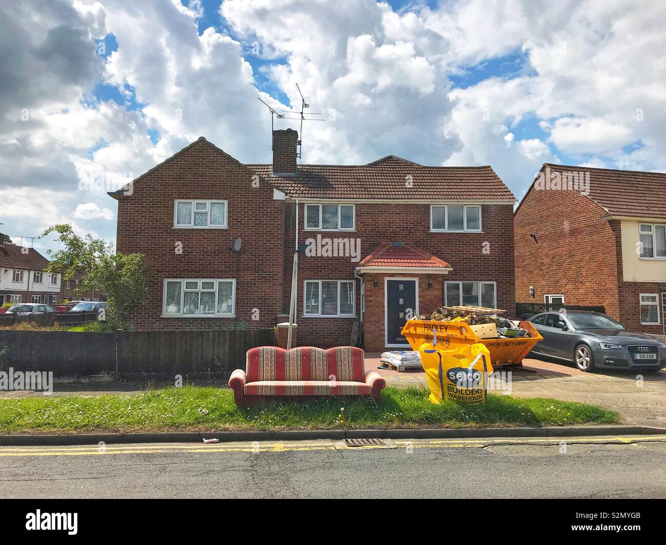 A house undergoing refurbishment with a skip on the drive and a bag of building materials and an old settee on the grass verge. Stock Photo