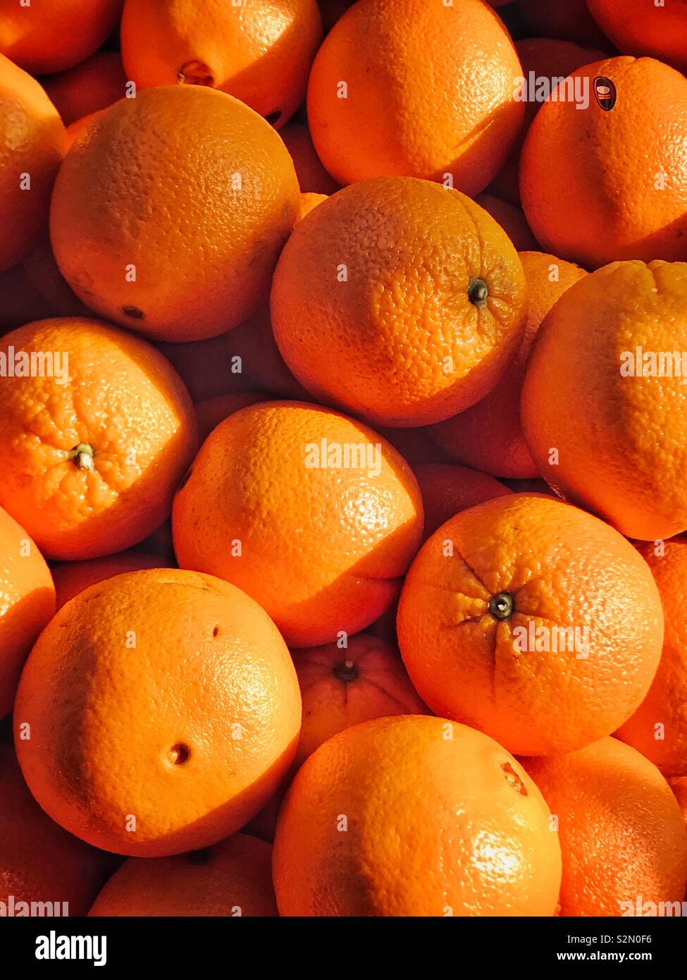 A pile of fresh Oranges for sale at a market stall. Succulent and inviting. Good or bad? A great source of vitamins OR acidic juices that attack your teeth and cause decay? Photo © COLIN HOSKINS. - Smartphone Captured Stock Image