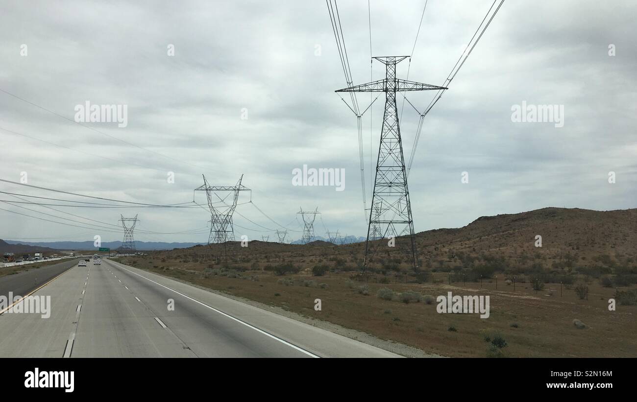 Power pylons and high voltage electric cables crossing freeway and disappearing into mountains, Apple Valley region, California. Overcast day - Smartphone Captured Stock Image