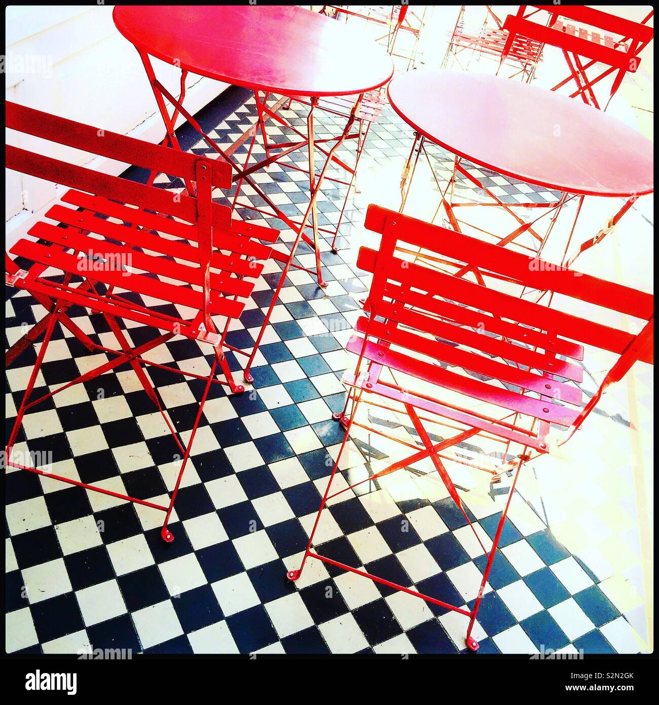 Red tables and chairs on black and white tiles. - Smartphone Captured Stock Image