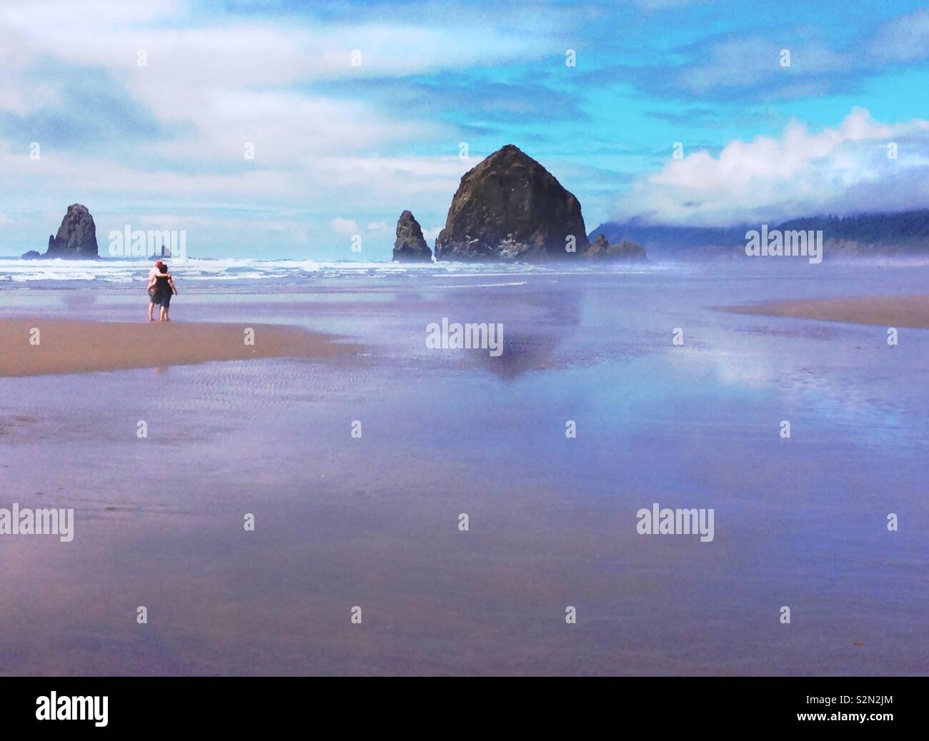 Couple walking together on the beach by Haystack Rock in Cannon Beach Oregon. - Smartphone Captured Stock Image