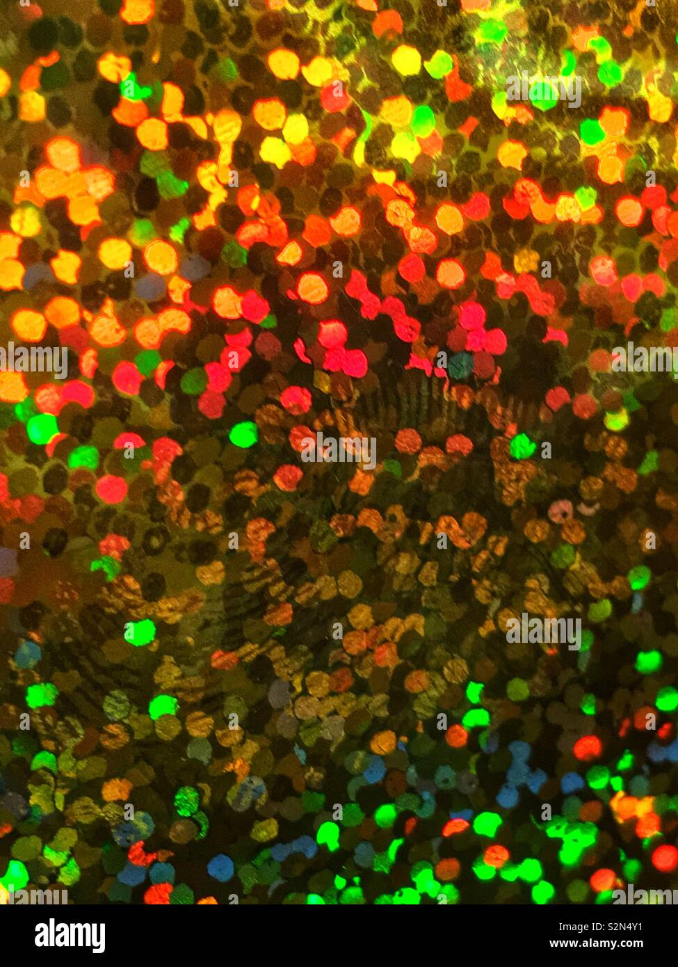 Bright blue, yellow, orange, and green colorful holographic, abstract, and prismatic arrangement of small tiny sequins  reflecting in the light. - Smartphone Captured Stock Image