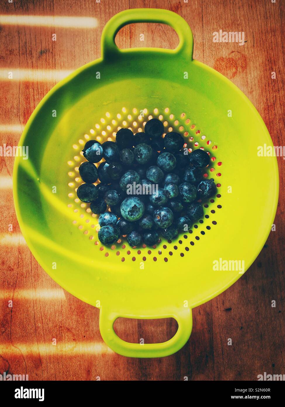 Freshly washed blueberries in a lime green colander with lines of sunlight - Smartphone Captured Stock Image