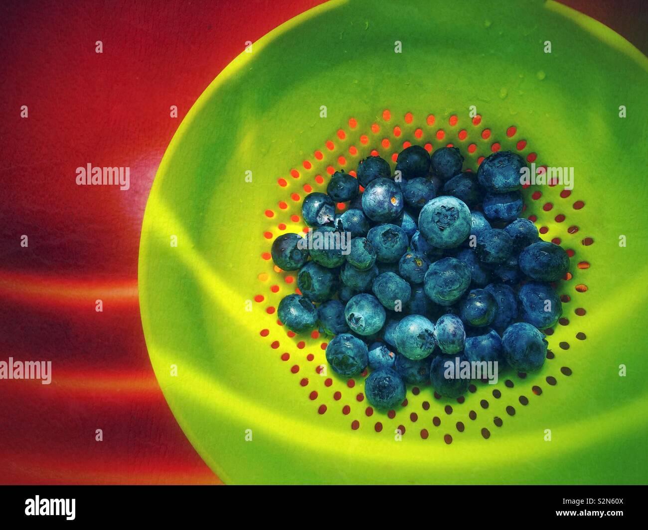 Freshly washed blueberries in a bright green plastic colander in an orange surface with lines of sunlight - Smartphone Captured Stock Image