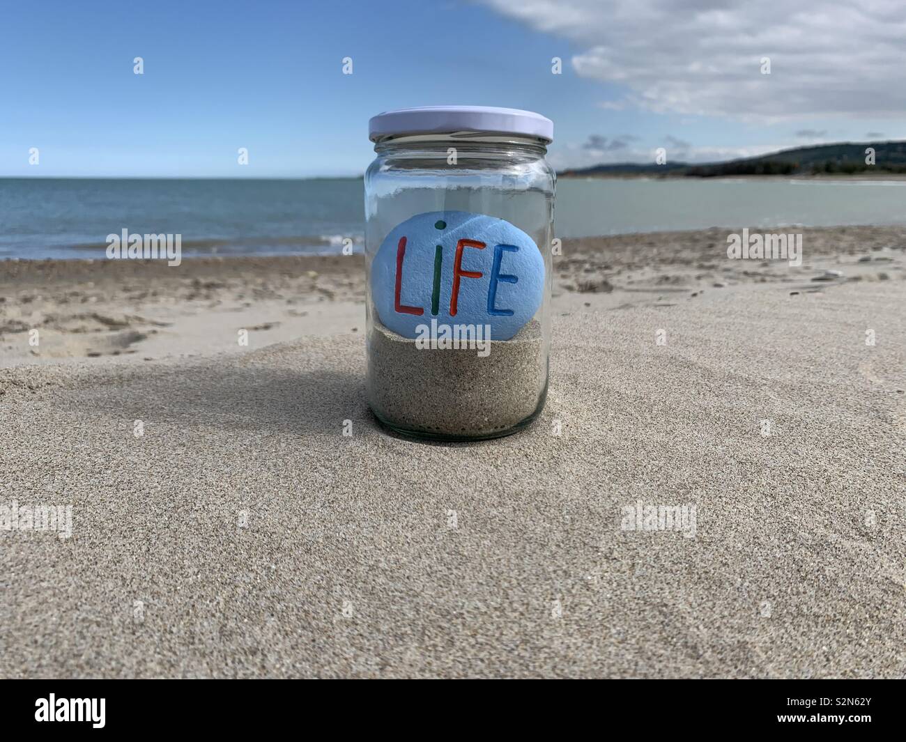 Life stone in a glass jar with sand over the beach - Smartphone Captured Stock Image