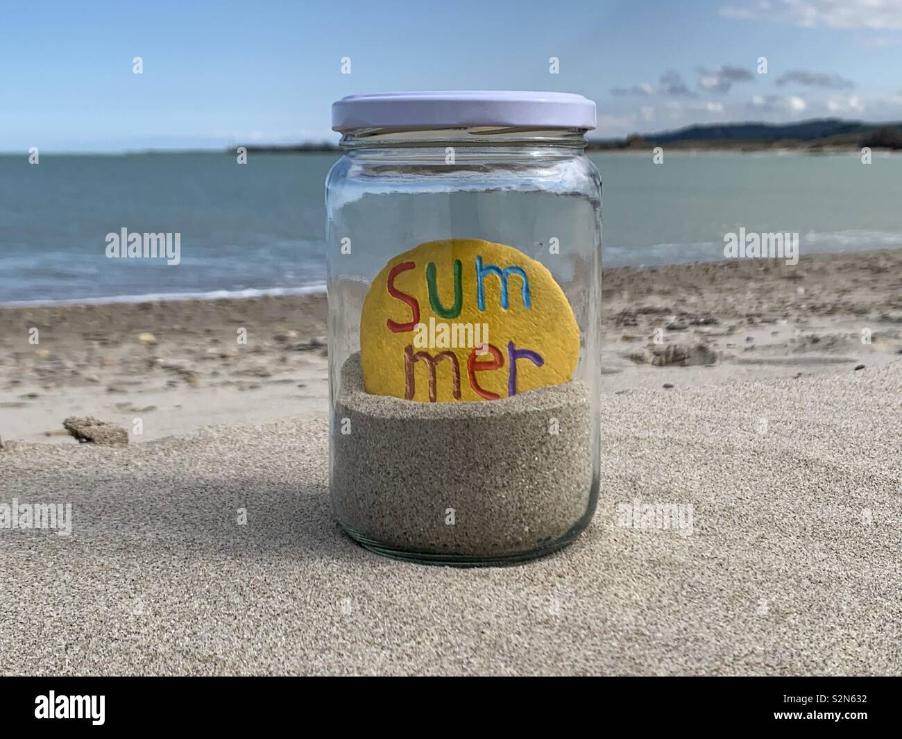 Summer stone in a glass jar with sand on the beach - Smartphone Captured Stock Image