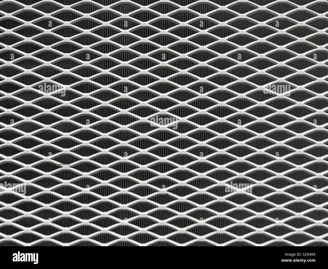 A gray metal protective grill is shown up close in front of a radiator. - Smartphone Captured Stock Image