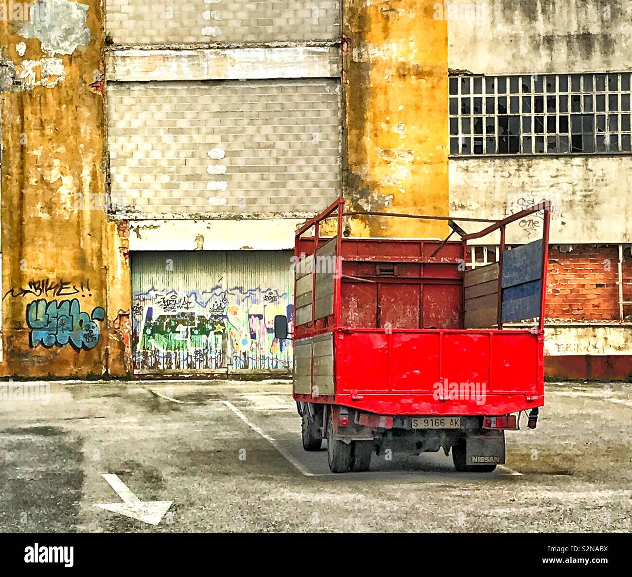 A red truck parked in front of a dilapidated warehouse with graffiti daubed on the walls in the fishing village of Santoña, northwest Spain Stock Photo