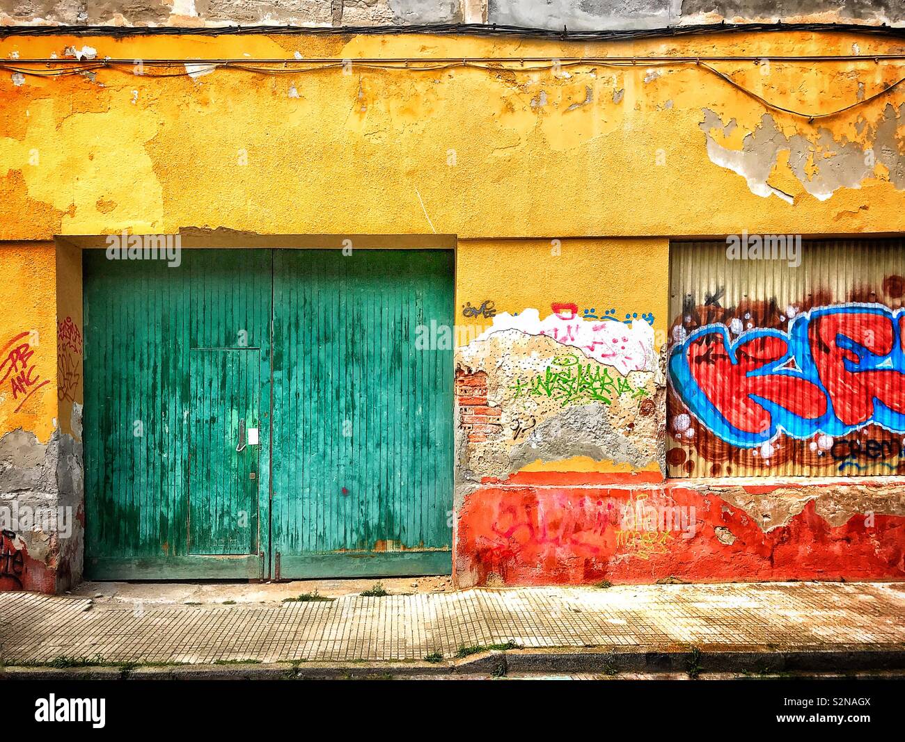 Green entrance doors to a dilapidated building in the Spanish fishing village of Santoña, the walls of which are daubed with graffiti. Stock Photo