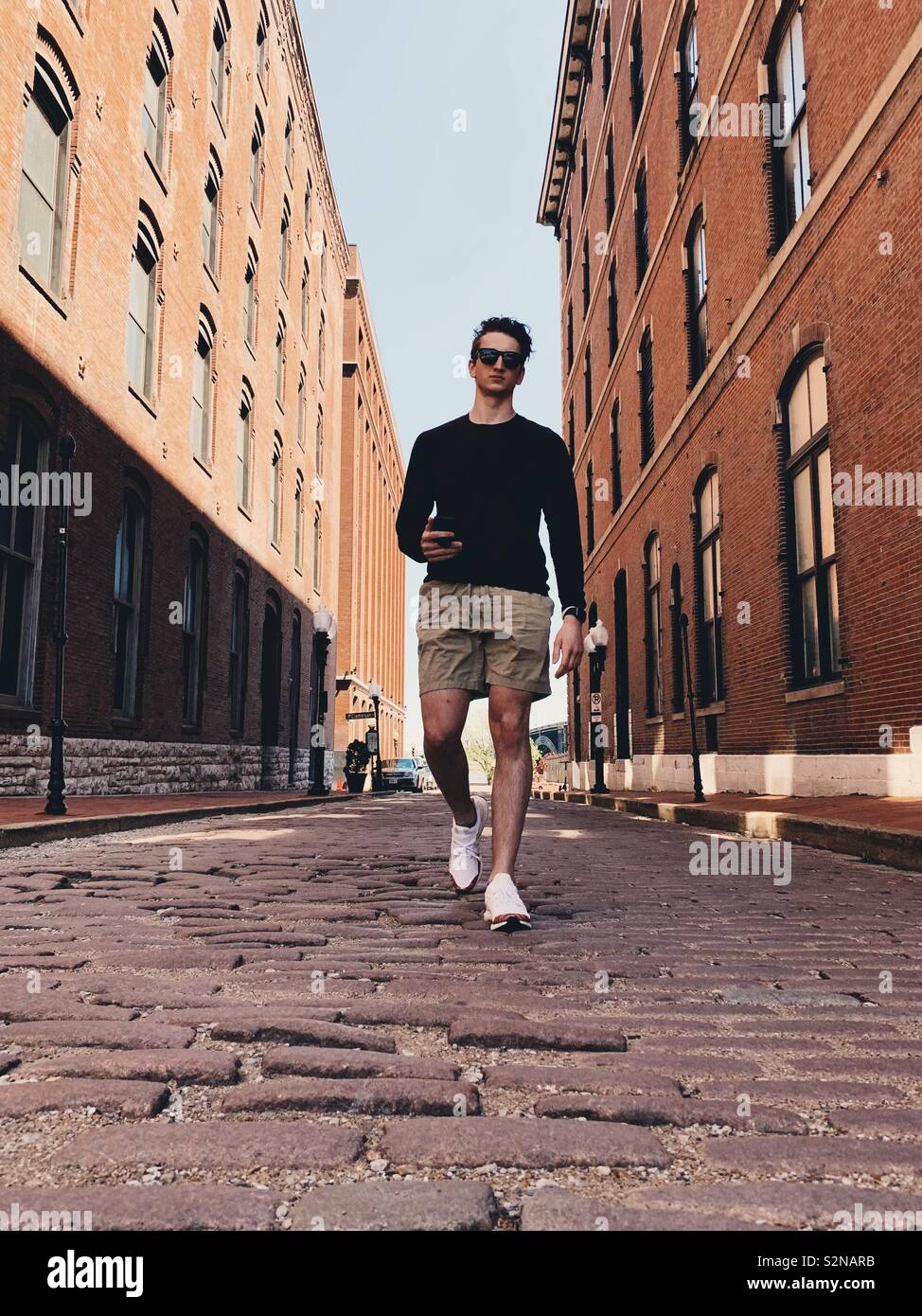 Young man walking in the middle of cobblestone street surrounded by brick buildings. - Smartphone Captured Stock Image Young man walking in the middle of cobblestone street surrounded by brick buildings. - Smartphone Captured Stock Image