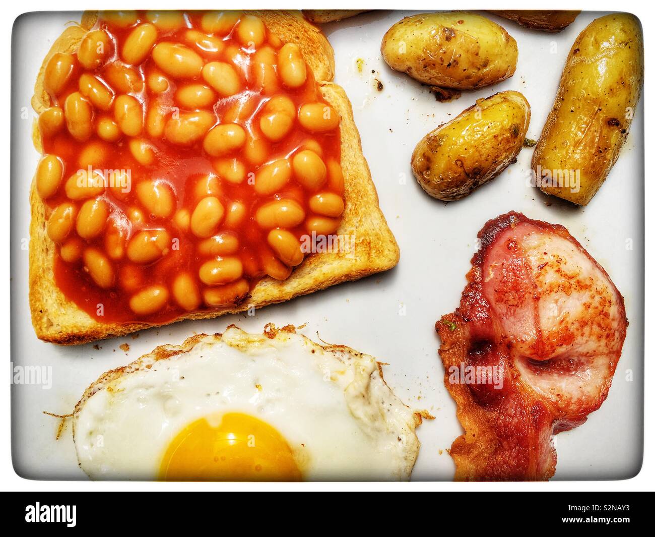 Beans on toast, bacon, fried potatoes and egg Stock Photo