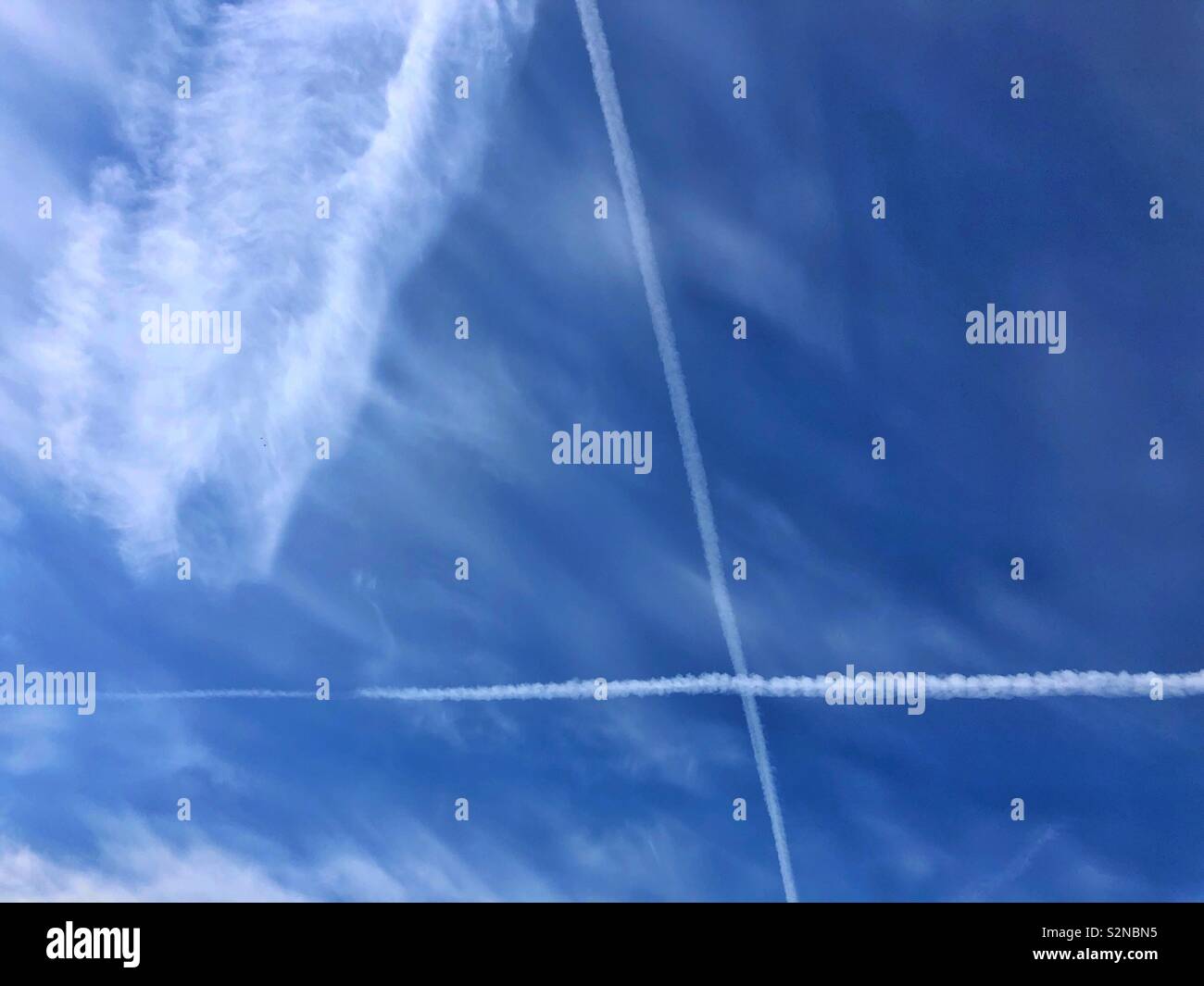 Big blue sky with high cirrus clouds and a big X from vapour trails. Stock Photo