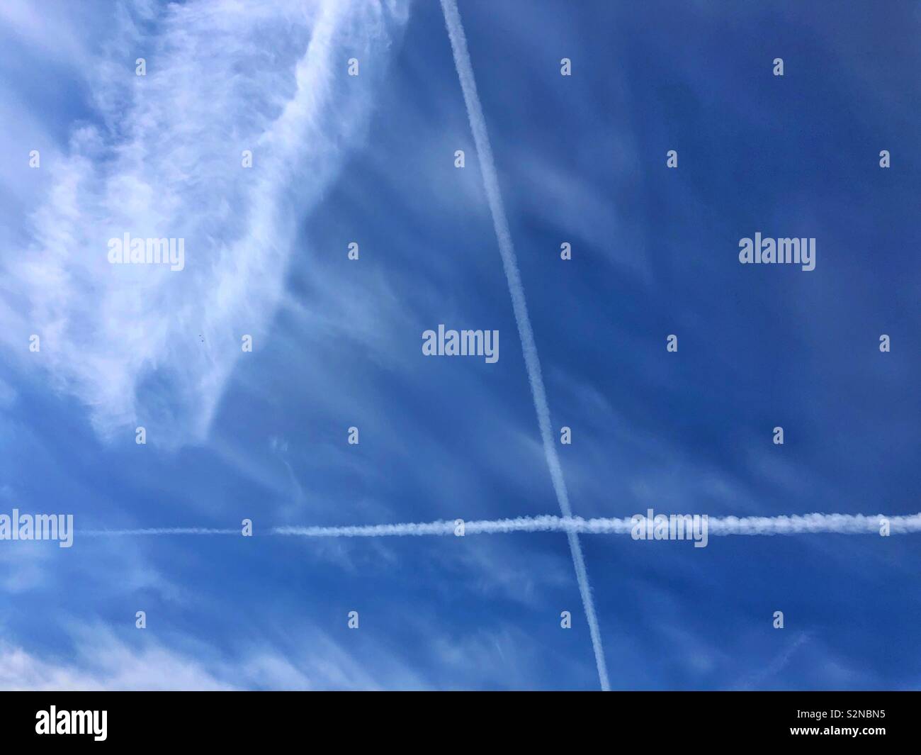 Big blue sky with high cirrus clouds and a big X from vapour trails. - Smartphone Captured Stock Image
