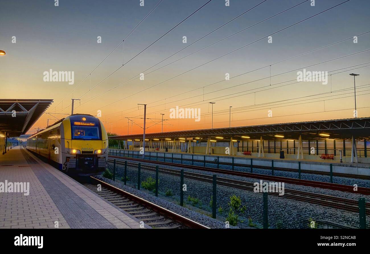 A train waiting in a small railway station in the morning or evening under a dramatic and colorful sunrise or sunset sky - Smartphone Captured Stock Image