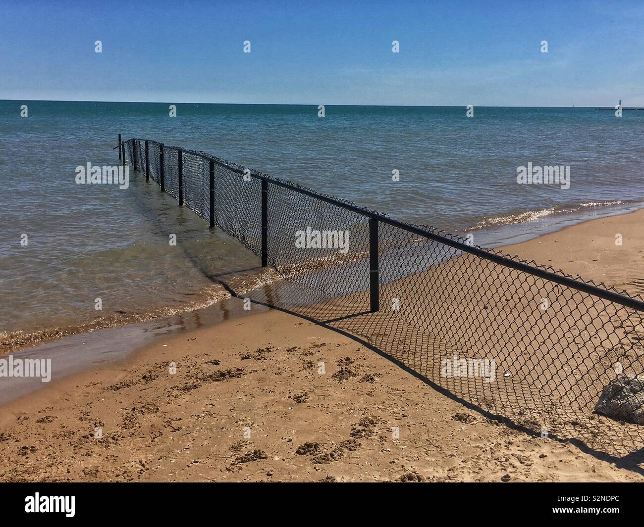 Black chain link fence going into Lake Michigan and separating two beaches. - Smartphone Captured Stock Image