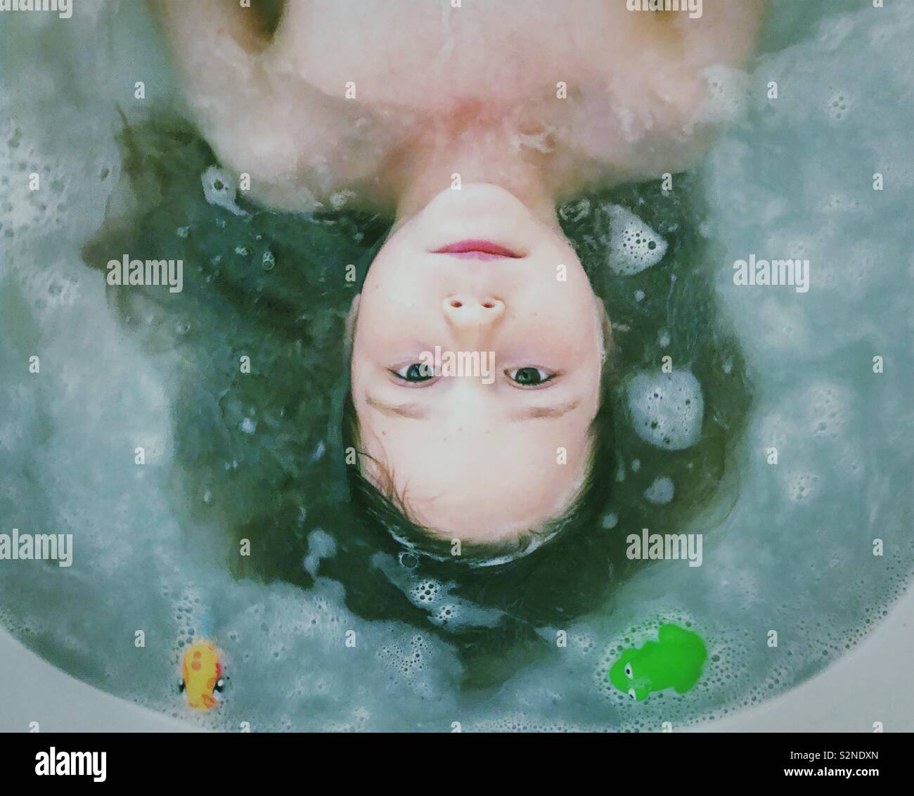 Young girl lying down partially immersed in bubble bath looking at