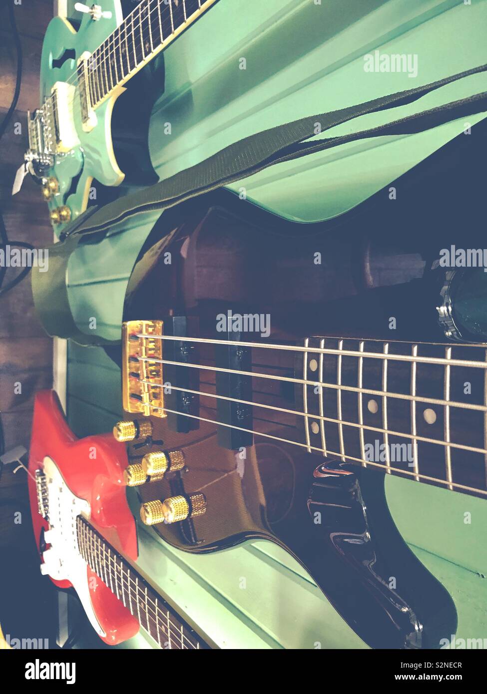 Matte photo looking down the mint green wall at three electric guitars