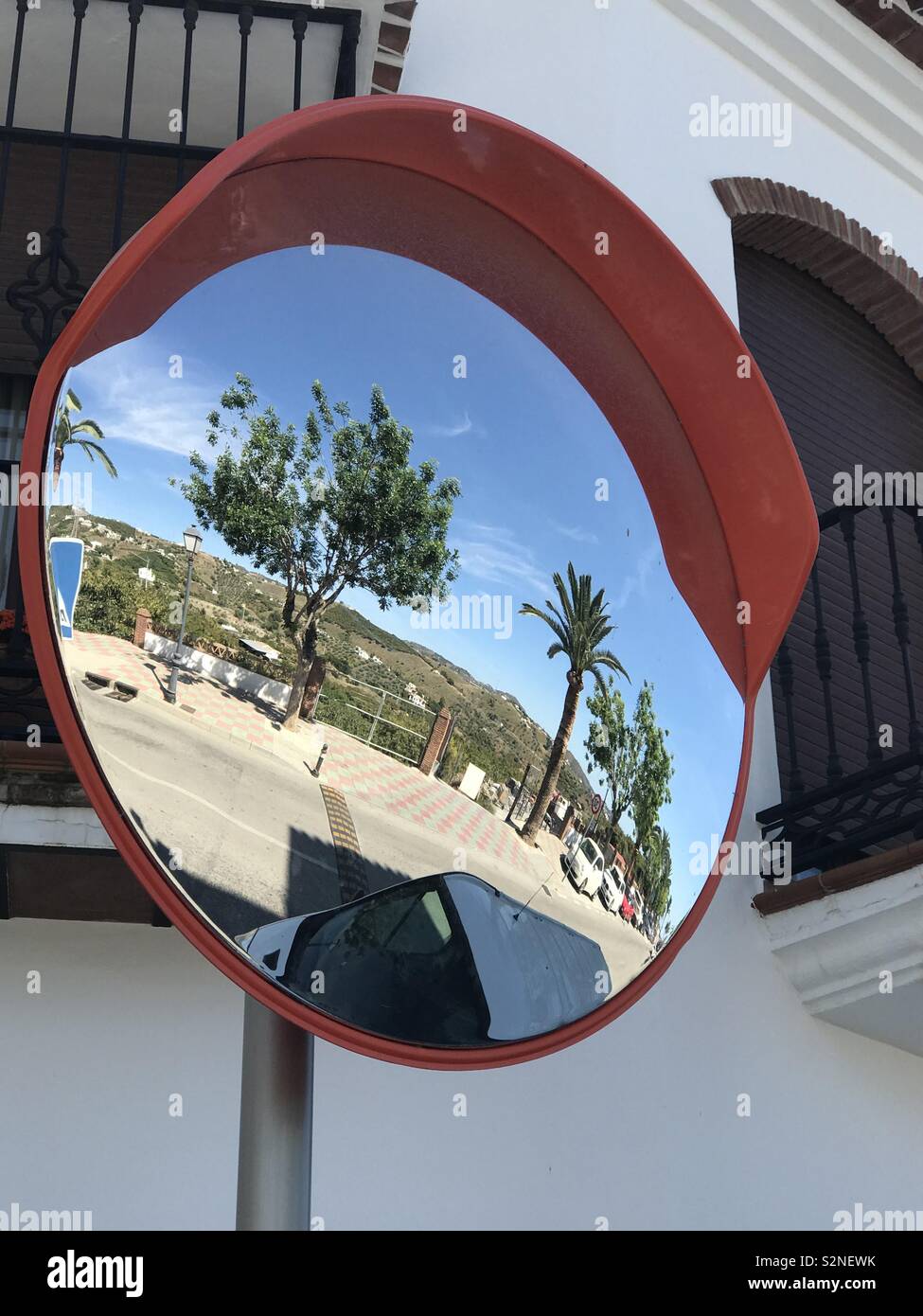 A traffic mirror in Frigiliana , Costa del Sol, Spain reflects a bright blue sky and palm trees. - Smartphone Captured Stock Image