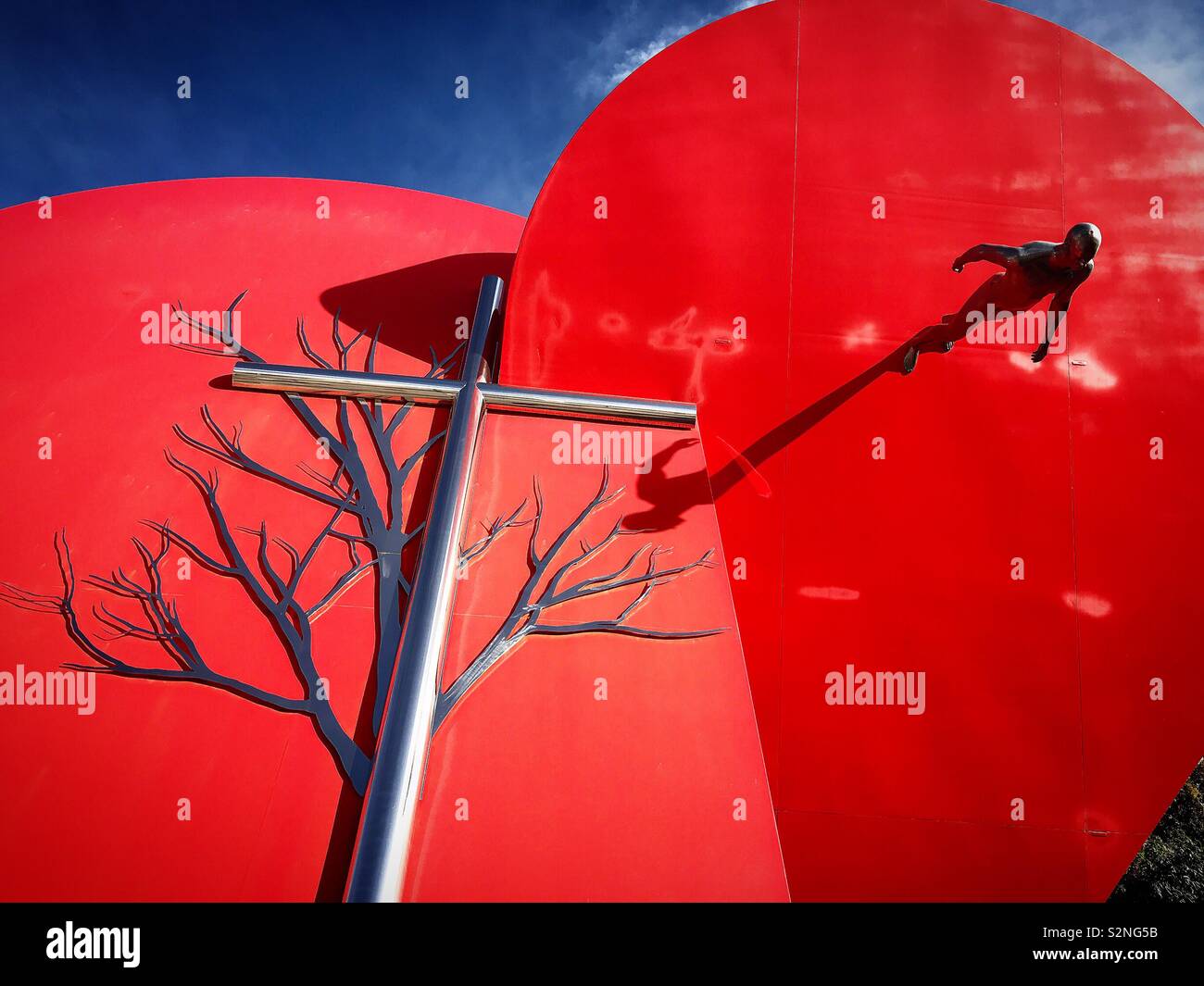 A tree, a cross and a sculpture of a human walking decorate a nir red heart monument in Fatima, Portugal - Smartphone Captured Stock Image