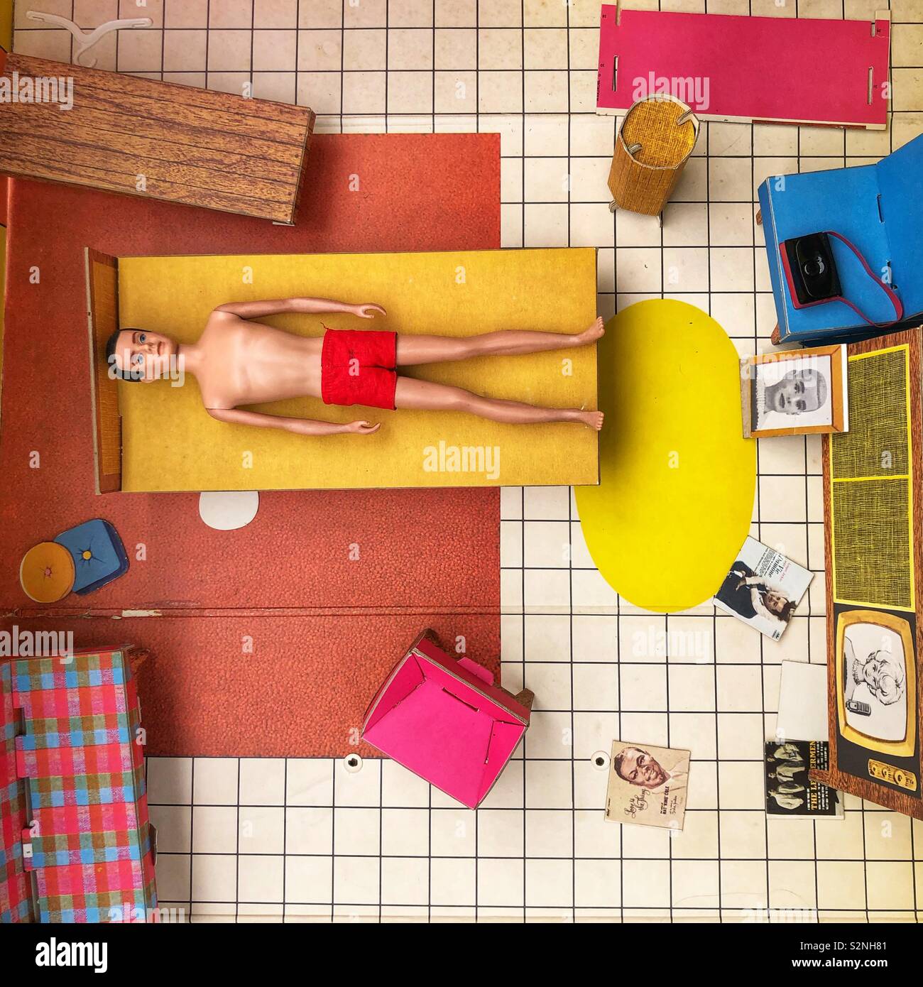 A Ken doll sleeps on a bed in a doll house from an aerial view Stock Photo