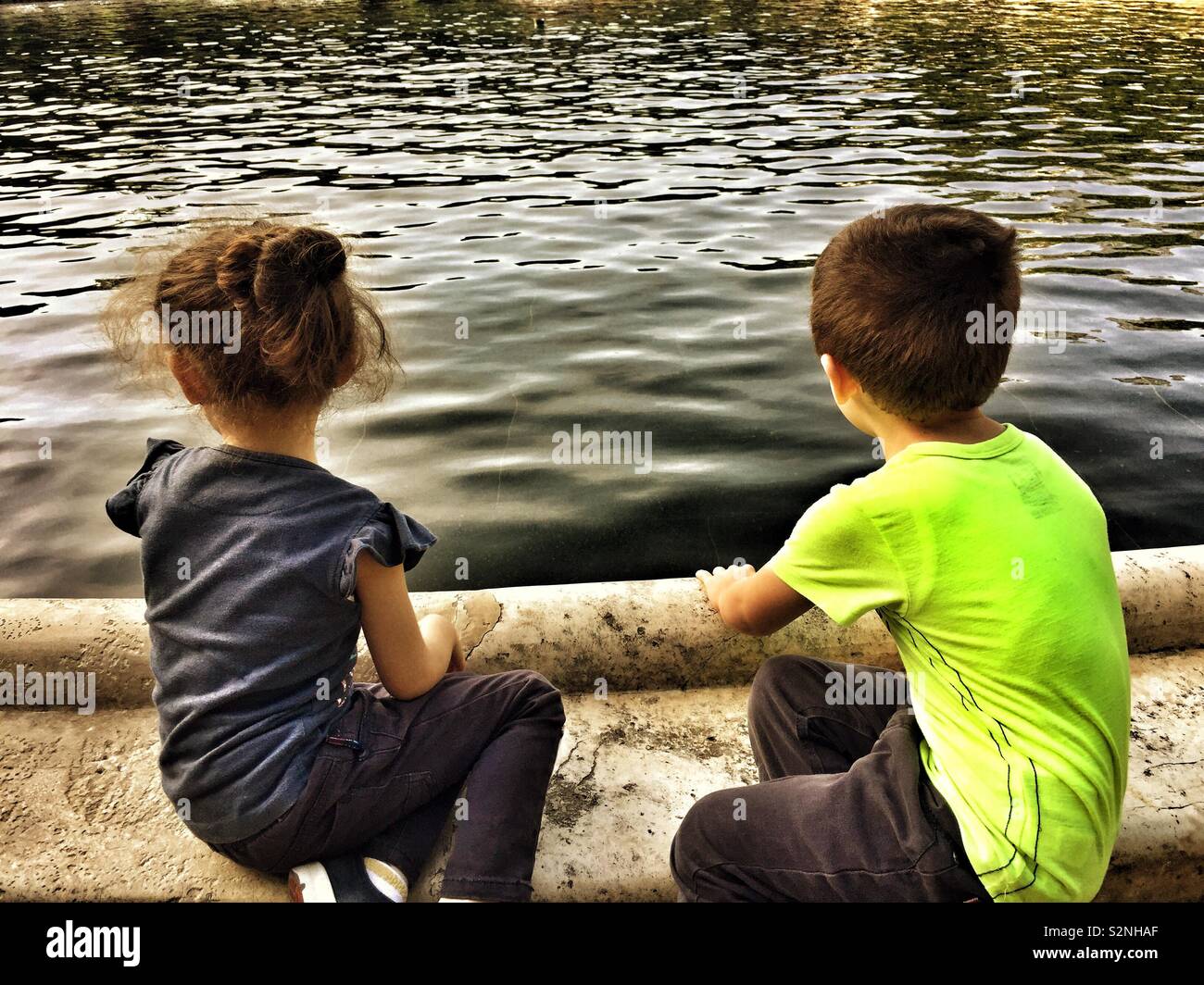 Boy and girl sitting by the water Stock Photo