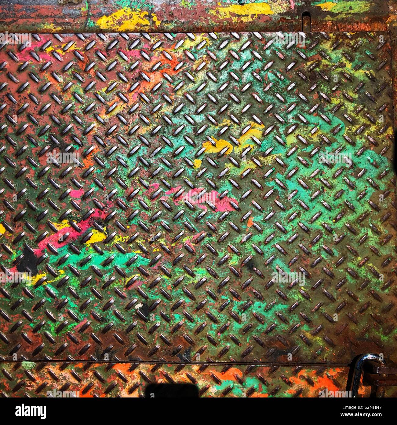 A metal door in a sidewalk splattered with colorful paint - Smartphone Captured Stock Image