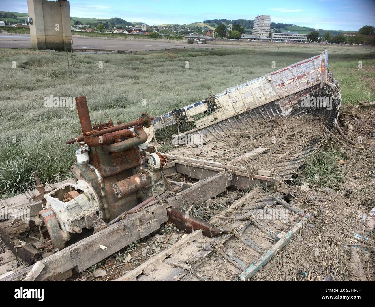 Wreck of a boat on the shoreline showing rusted engine and wooden framework. In the distance is a bridge over the river. River Taw Devon - Smartphone Captured Stock Image