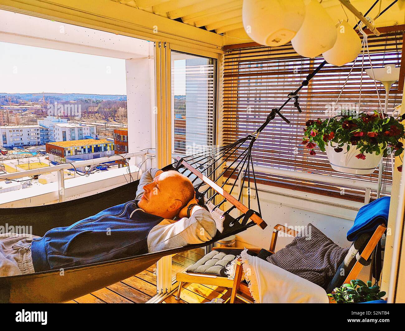Handsome mid adult man lying in hammock on high rise apartment terrace, Sweden, Scandinavia - Smartphone Captured Stock Image
