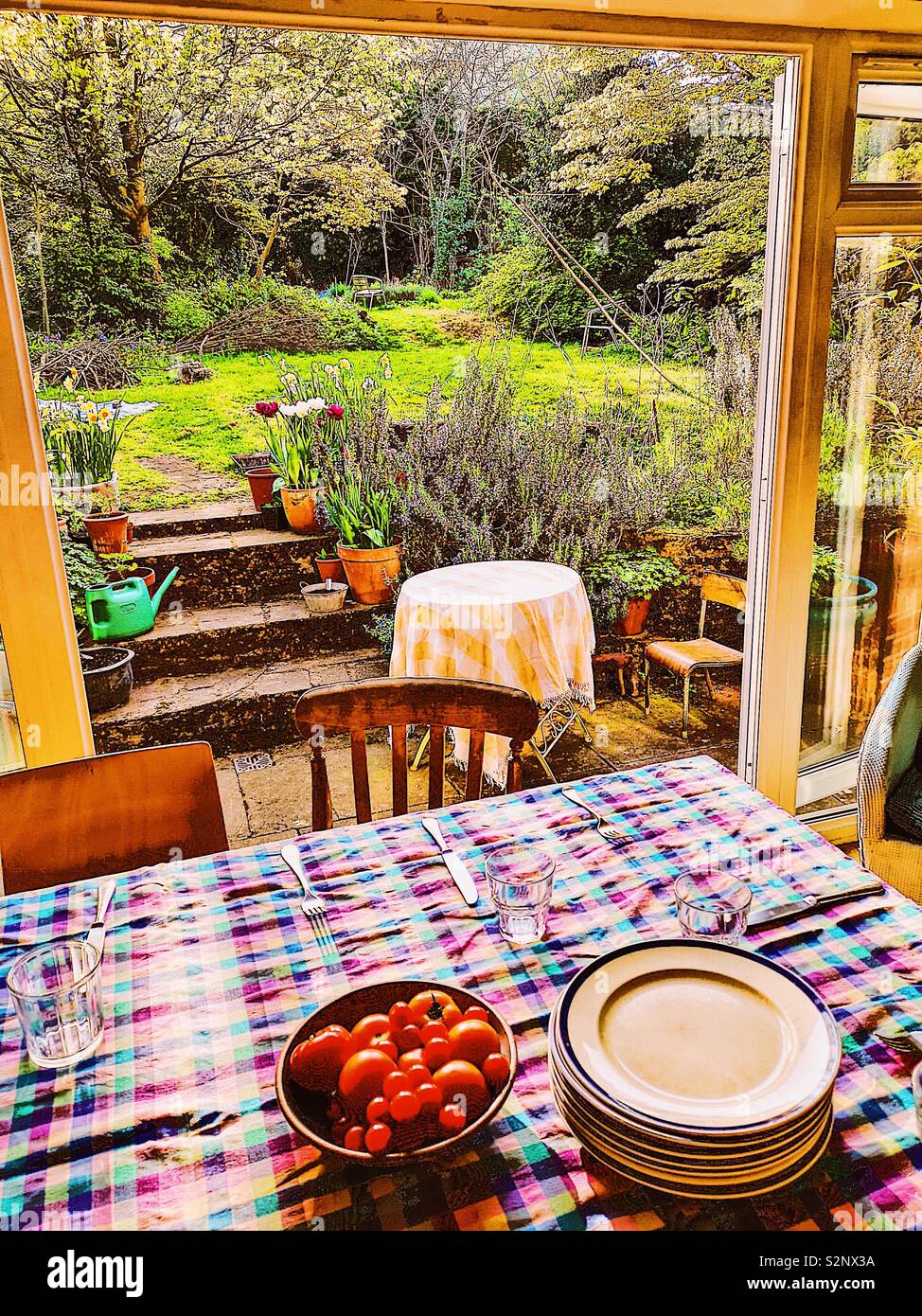 Table with bowl of fresh tomatoes and view through doors to garden - Smartphone Captured Stock Image
