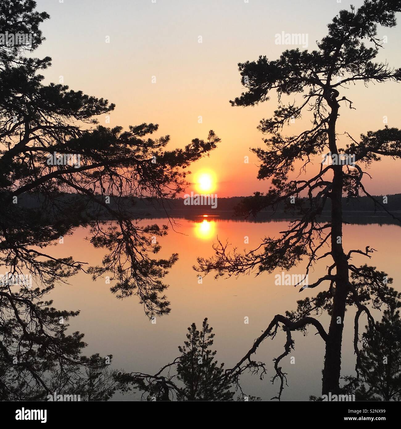 Sun setting in the Scandinavian archipelago over a small strip of sea, on the other side there is another island. Stock Photo