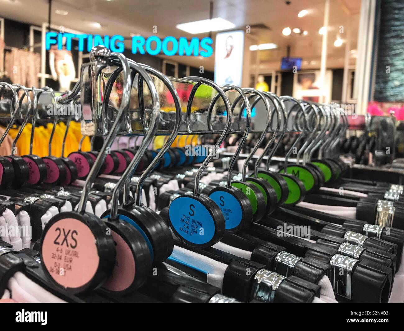Clothes hangers on a rail in a clothes shop are colour coded for different sizes. - Smartphone Captured Stock Image
