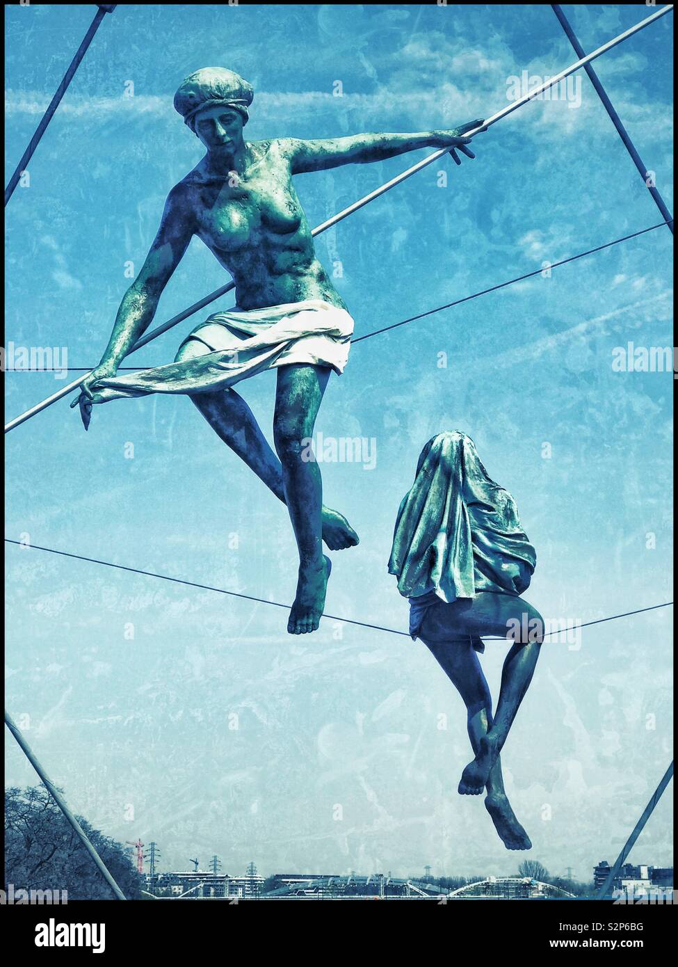 Two of the famous acrobatic sculptures balancing above the Father Bernatek Footbridge & Vistula River in Kraków, Poland. Created by Jerzy Kędziora. Photo © COLIN HOSKINS. - Smartphone Captured Stock Image