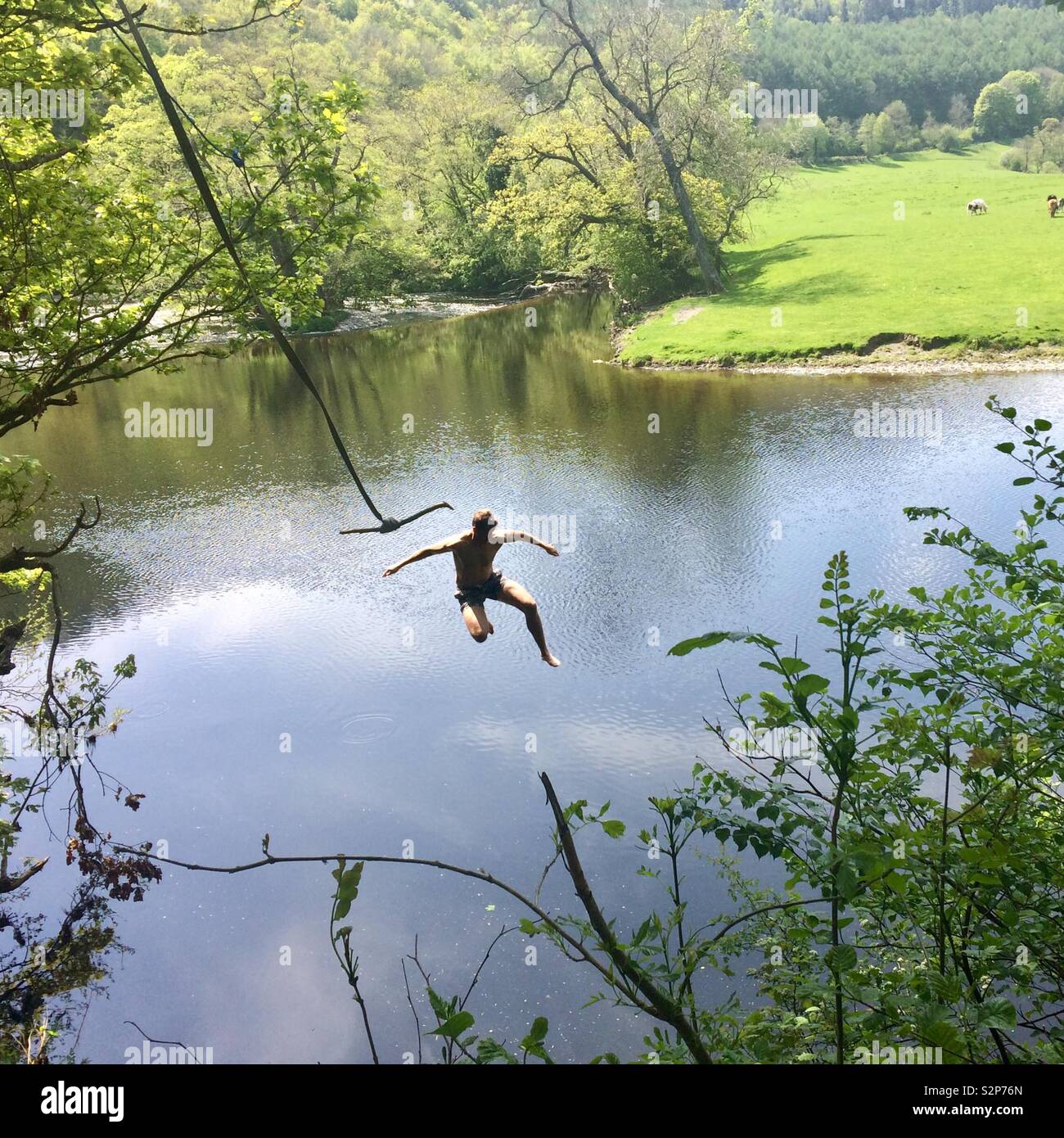 Leap of faith: Single figure leaving swing to drop into river on a sunny day Stock Photo