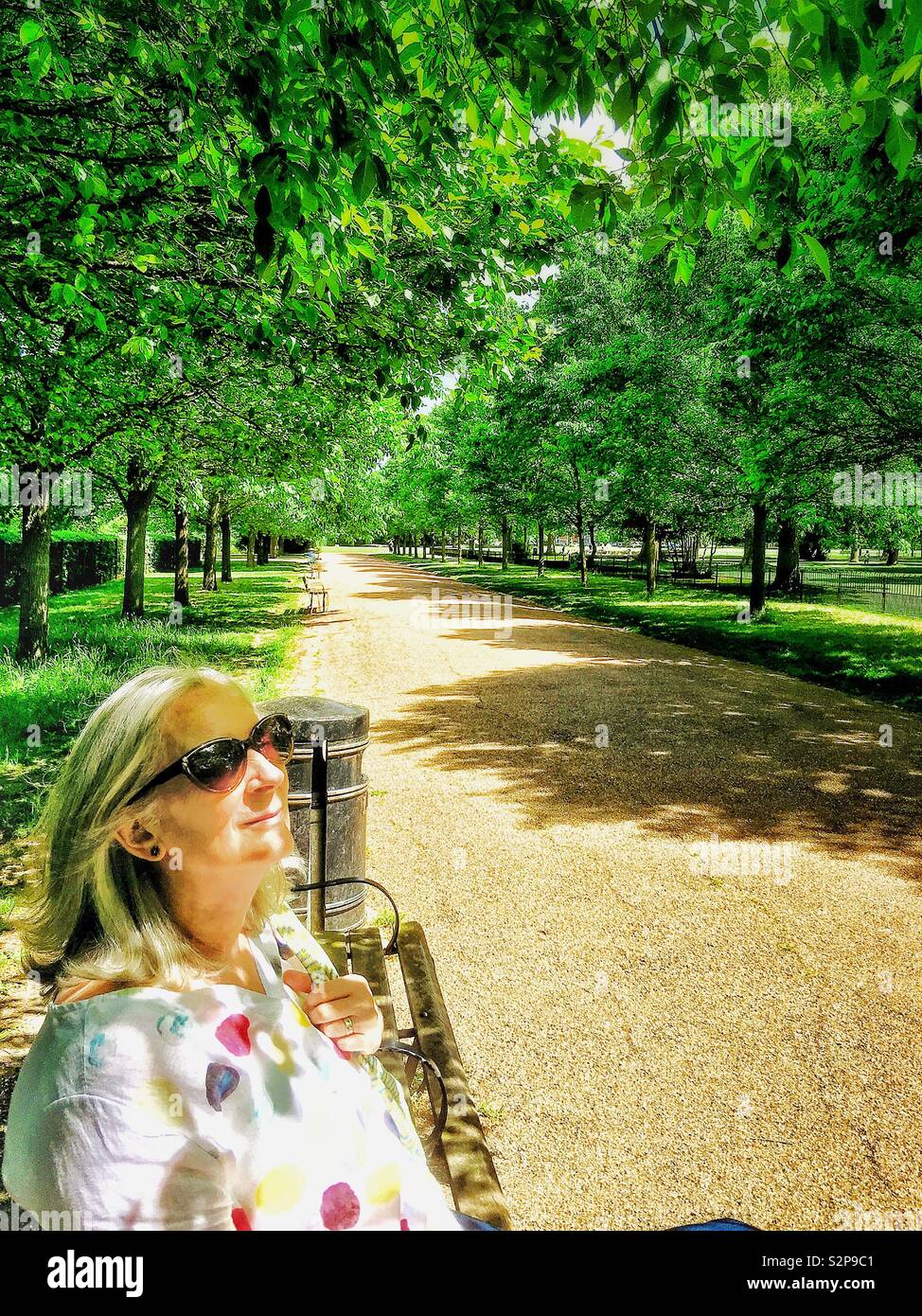 A mature woman enjoying the sun, sitting in a park. - Smartphone Captured Stock Image