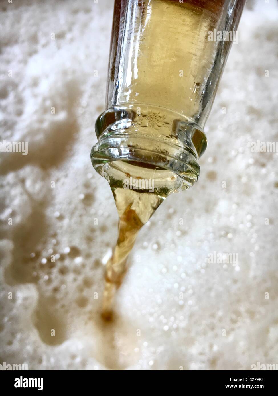 Lager beer being poured from a bottle resulting in a large amount of froth Stock Photo